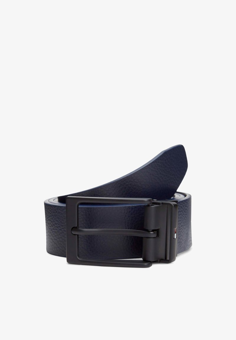 Ceinture en cuir bleu foncé roulée avec une boucle rectangulaire noire et un petit détail de drapeau rouge, blanc et bleu sur le côté.