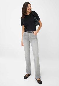 Grijze flared jeans met een gladde textuur, gecombineerd met een zwart t-shirt met korte mouwen. Een zwarte riem en een gestructureerde zwarte tas zijn inbegrepen.