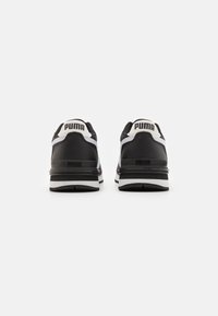 Zapatillas deportivas en blanco y negro con un upper de cuero texturizado, cuello acolchado y acentos de logo en el talón y en los paneles laterales.