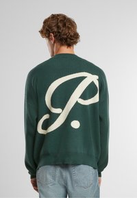 Dunkelgrüner Strickpullover mit großem cremefarbenen "P."-Logo auf dem Rücken, Rundhalsausschnitt und gerippten Bündchen. Lässiges Design mit lockerer Passform.