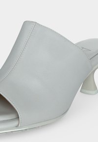 Ανοιχτόγκρι παπούτσι mule με λείο δερμάτινο επάνω μέρος και καμπυλωτό, τετράγωνο τακούνι σε λευκό φόντο.