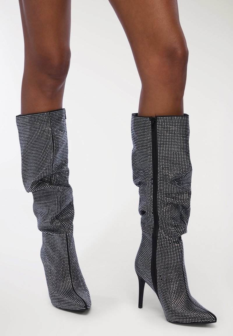 Stivali neri con strass, al ginocchio, dal design slouchato, con punta appuntita e alto tacco a stiletto; con chiusura centrale a cerniera.