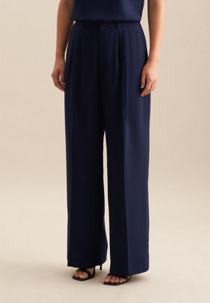 Donkerblauwe wijde broek in een gladde stof, met voorplooien en een hoge taille. Gecombineerd met zwarte hoge hakken sandalen.