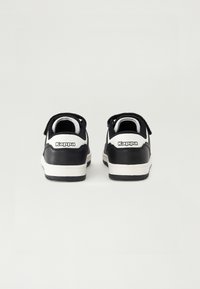 Sapatilhas pretas e brancas com um cabedal de couro liso, calcanhar branco em contraste e um colarinho almofadado. Apresenta um logótipo Kappa em destaque na parte de trás.