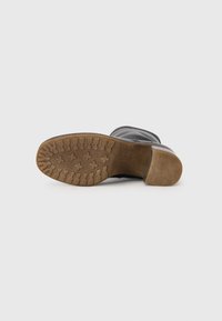 Botte en cuir noir avec une semelle en caoutchouc brun texturé présentant un motif de marche et un talon courbé. Dessus lisse et design de bout arrondi.