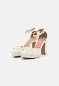 Weisse hochhackige Schuhe mit runder Zehenpartie, verziert mit Perlen- und Strass-Applikationen auf der Vorderseite sowie einem Knöchelriemen zur Unterstützung.