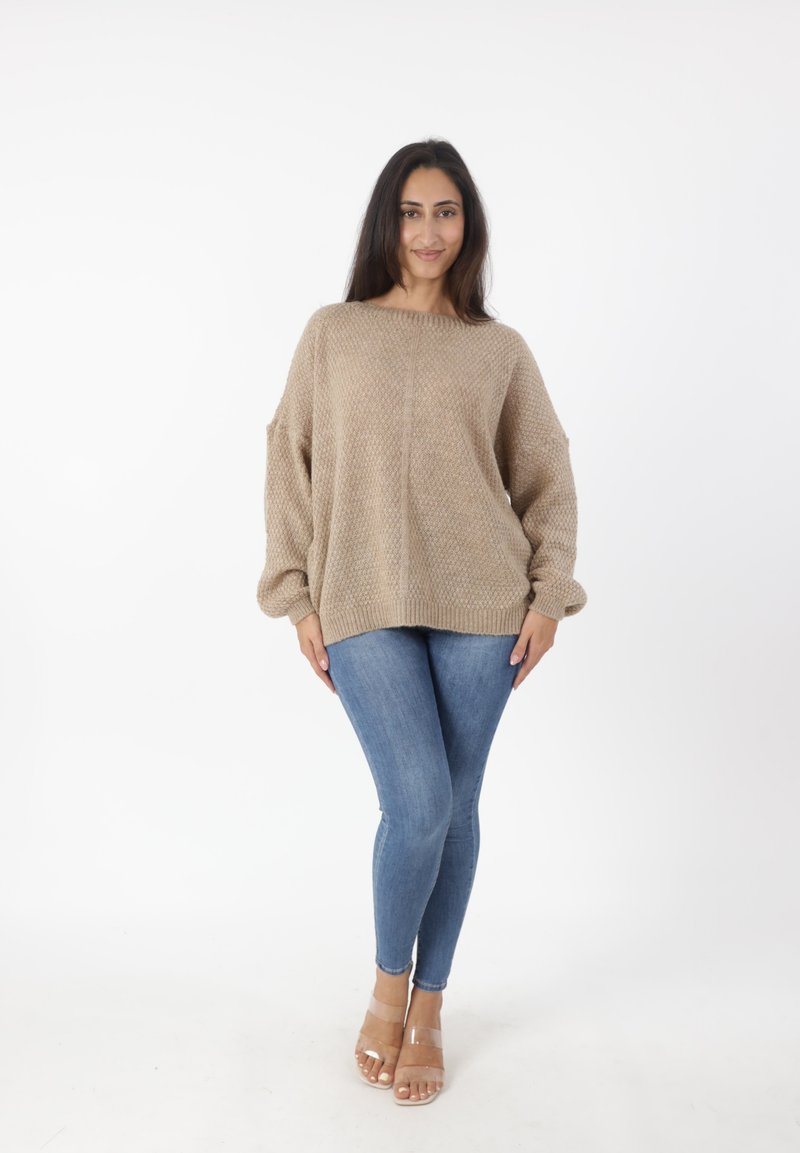 Beige oversized gebreide trui met een textuurpatroon, gecombineerd met strakke blauwe jeans en doorschijnende blokhak sandaaltjes. Eenvoudig, ontspannen ontwerp.