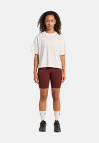 Hvid oversized t-shirt med korte ærmer, kombineret med burgunder cykelshorts. Sorte træningssko og hvide sokker. Krøllet hår.