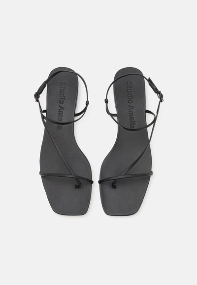 Mustat sandaalit littealla pohjalla, ohuilla hihnoilla, jotka ristivät jalkapöydän päällä, minimalistinen muotoilu sileällä pinnalla.