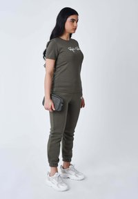 Camiseta verde oliva y joggers a juego de tejido suave, con un logo blanco en la camiseta. Combinado con zapatillas blancas y un bolso de mano estampado.
