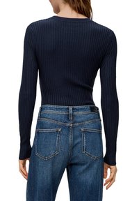 Marineblaues, geripptes Langarmoberteil mit Rundhalsausschnitt, kombiniert mit hochgeschnittenen blauen Denim-Jeans, die über Gesäßtaschen und dezente Nähten verfügen.
