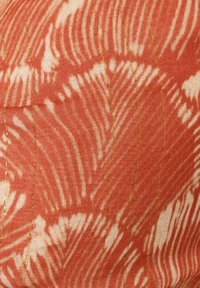 Tela roja con patrones abstractos ondulados en blanco, con líneas de costura doradas para textura y detalle. Acabado de superficie suave.