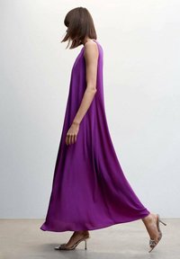 Robe maxi sans manches violette avec une silhouette fluide, en tissu léger ; associée à des chaussures à talons hauts métalliques.