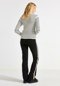 Sort og hvid stribet, ribbet striktrøje med lange ærmer, båret med sorte bukser med en gylden sideliste.