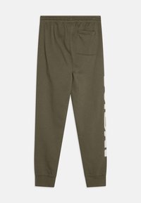 Pantaloni de trening verzi măslinii cu talie ajustabilă, buzunar lateral și imprimeu grafic alb pe partea stângă; realizați dintr-un material moale și elastic.