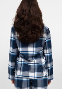 Niebiesko-szara flanelowa piżama w kratę z długimi rękawami i prostym krojem, charakteryzująca się miękką teksturą i białymi detalami.