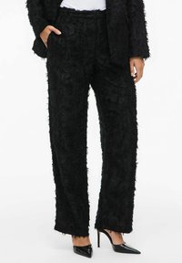 Black textured wide-leg trousers with a frayed finish, featuring side pockets and a relaxed fit, paired with pointed black heels.