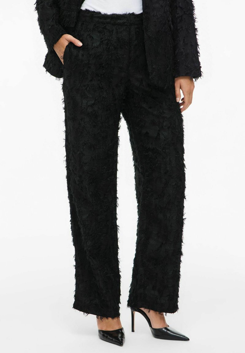 Black textured wide-leg trousers with a frayed finish, featuring side pockets and a relaxed fit, paired with pointed black heels.