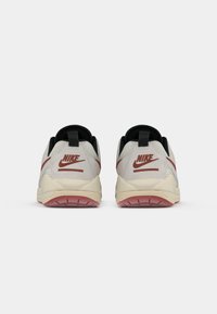 Sneakers Nike bianchi e grigi con una parte superiore testurizzata, accenti neri, logo swoosh rosso e una suola intermedia beige. La vista posteriore mostra un design distintivo del tallone.