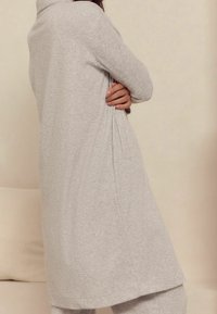 Grijze gebreide lange cardigan met ribbeltextuur, voorzien van een hoge halslijn, zijplooien en een relaxte pasvorm, die tot halverwege de kuit reikt.