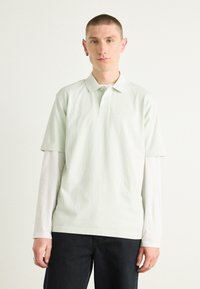 Licht mintgroen polo shirt van zacht katoen, korte mouwen, kraag, gedragen over een wit longsleeve shirt, in combinatie met donkere broek.