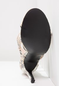 Chaussure à talon haut avec semelle noire et motif en peau de serpent, vue par le dessous avec talon visible et semelle texturée.