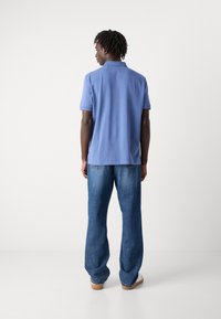 Lys blå kortermet polo skjorte sett fra baksiden, kombinert med løstsittende blå denim jeans og uformelle sko.