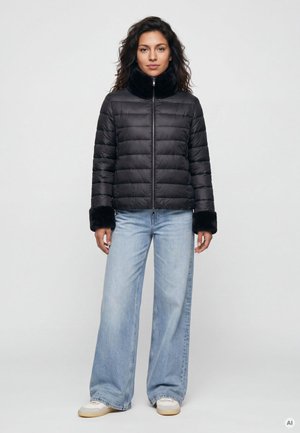 Frau trägt eine schwarze Steppjacke mit Pelzkragen und -manschetten, hellblaue Jeans mit weitem Bein und weiße Sneaker, steht vor einem einfarbigen Hintergrund.