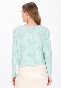 Heller mintgrüner Strickpullover mit cropped Design, der ein Rautenmuster und offene Maschen aufweist, kombiniert mit einem cremefarbene Rock.