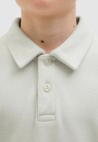 Ljusgrå polo t-shirt med en texturerad tyg, tre knappar vid kragen, och en mjuk, bekväm krags detalj.