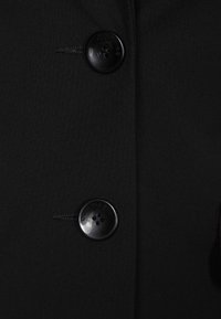 Tissu noir, vue rapprochée d'un vêtement à boutons. Comprend des boutons noirs avec une finition brillante et des détails de couture.