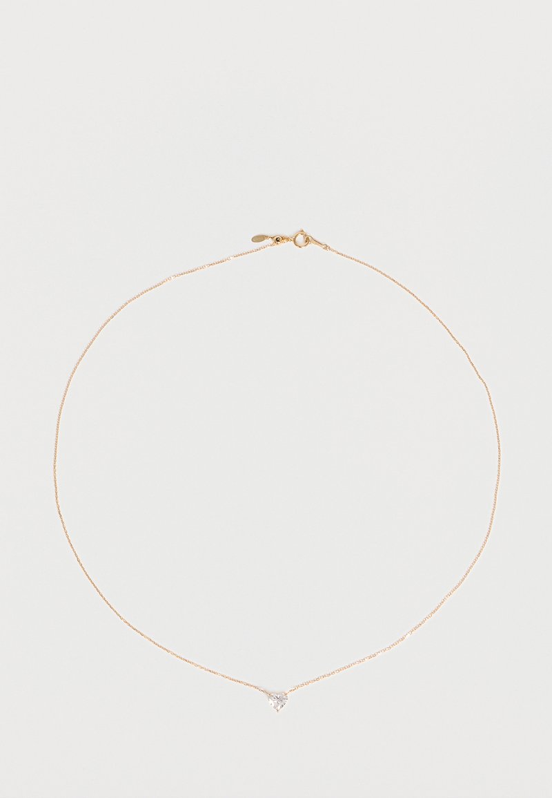 Collier délicat en chaîne d’or avec un petit pendentif translucide en forme de cœur centré sur un fond blanc uni.