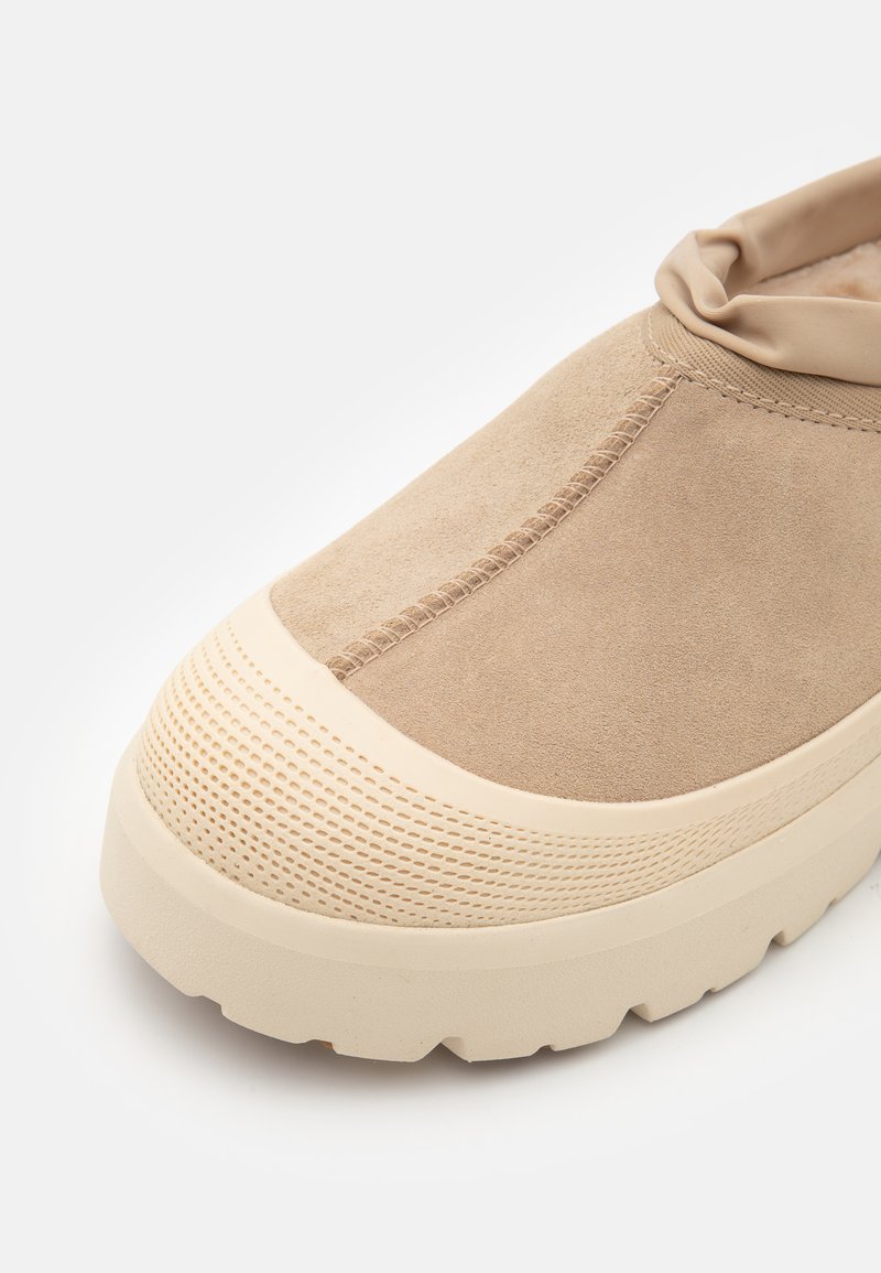 Baskets en suède beige avec une épaisse semelle en caoutchouc crème, des accents texturés et un col en élastique décontracté pour un ajustement sûr.