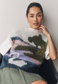 Pull en tricot présentant un motif de cygne et de paysage aux teintes pastel de rose, vert et bleu, avec des manches courtes blanches et un col rond.