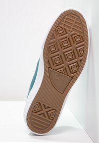 Semelle de basket en toile verte avec une semelle extérieure en caoutchouc marron. Présente des motifs texturés et le logo "Converse All Star" embossé. Accent sur la semelle intermédiaire blanche.