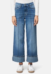 Szerokie dżinsy w jasnoniebieskim kolorze z wyblakłym wykończeniem, z przodu i z tyłu kieszeniami, pionowymi szwami oraz podwiniętymi mankietami.