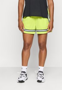 Neon grønne sportsshorts med sort og hvid striber. Båret med en sort top og hvide sokker, parret med sorte og hvide sneakers.