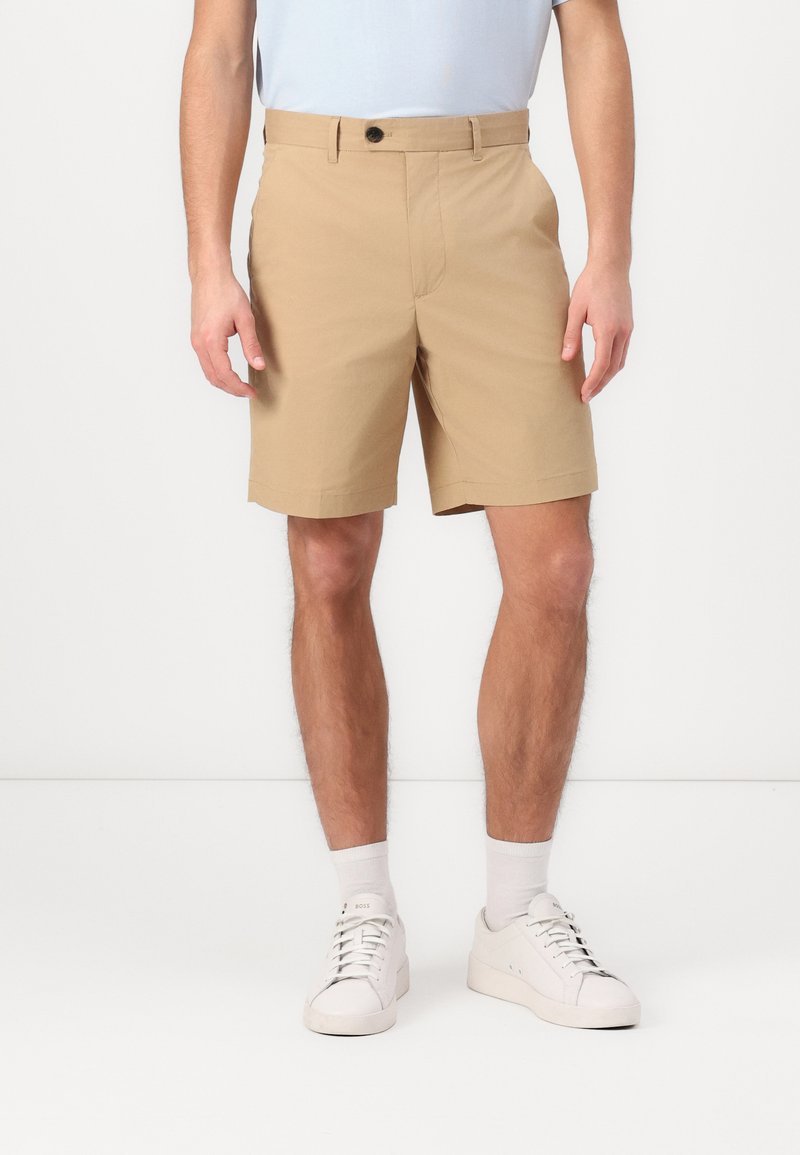 Pantaloni scurți chino kaki cu închidere cu buton, design plat în față, buzunare laterale și o croială regulară, asortați cu adidași albi și șosete.