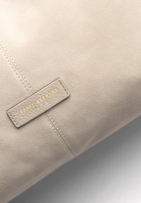 Sac en cuir beige avec une surface texturée, des détails de couture subtils, et une étiquette embossée en or avec "ISABEL BERNARD PARIS."