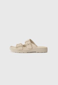 Beige sklisandaler med to justerbare spenner, semsket overdel og teksturert gummisåle, designet for komfort og støtte.
