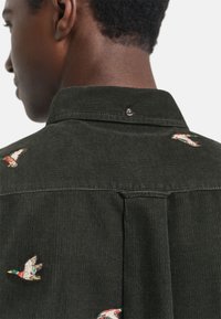Donkergroene corduroy shirt met geborduurde eenden, een puntige kraag en een drukknoop aan de achterkant van de halslijn.