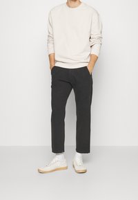 Felpa beige chiaro con un motivo testurizzato, abbinata a pantaloni cropped neri. Le calzature includono sneakers bianche con suole color beige chiaro.