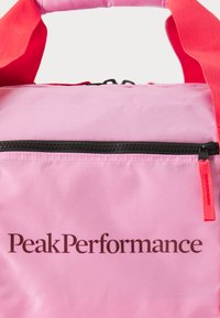 Rózsaszín textil táska piros pántokkal, fekete cipzárral. A "PeakPerformance" márkaneve sötétbarna színben van nyomtatva.