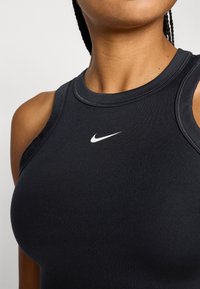 Musta urheilullinen hihaton paita, jossa on istuva malli, pyöreä pääntie ja pieni valkoinen Nike-logo rinnassa. Sileä tekstuuri.