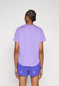 Μωβ αθλητική μπλούζα με στρογγυλή λαιμόκοψη, κοντά μανίκια και λείο υφή, σετ με μωβ σορτς που έχουν δύο λευκές βούλες.