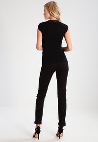 Top nero aderente con maniche corte e dettagli in pizzo sul collo, abbinato a jeans skinny neri e sandali con tacco alto.