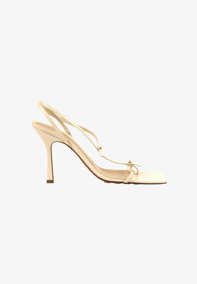 Sandale beige à talon haut avec fines brides, détails en perles dorées, bout carré et design à bride arrière.