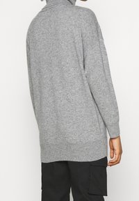 Grå, stickad polo tröja med lös passform, med långa ärmar och rak fåll. Mjuk textur, minimalistisk design och inga synliga mönster.