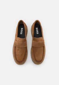 Mocassins en daim marron avec un bout rond, des coutures apparentes, et une semelle en caoutchouc contrastée. Logo "BOSS" visible sur la semelle intérieure.