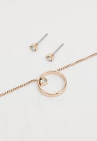 Un ensemble de bijoux en or rose comprend des boucles d'oreilles en forme de cœur avec des pierres transparentes et un collier assorti avec un détail en cœur et une chaîne.